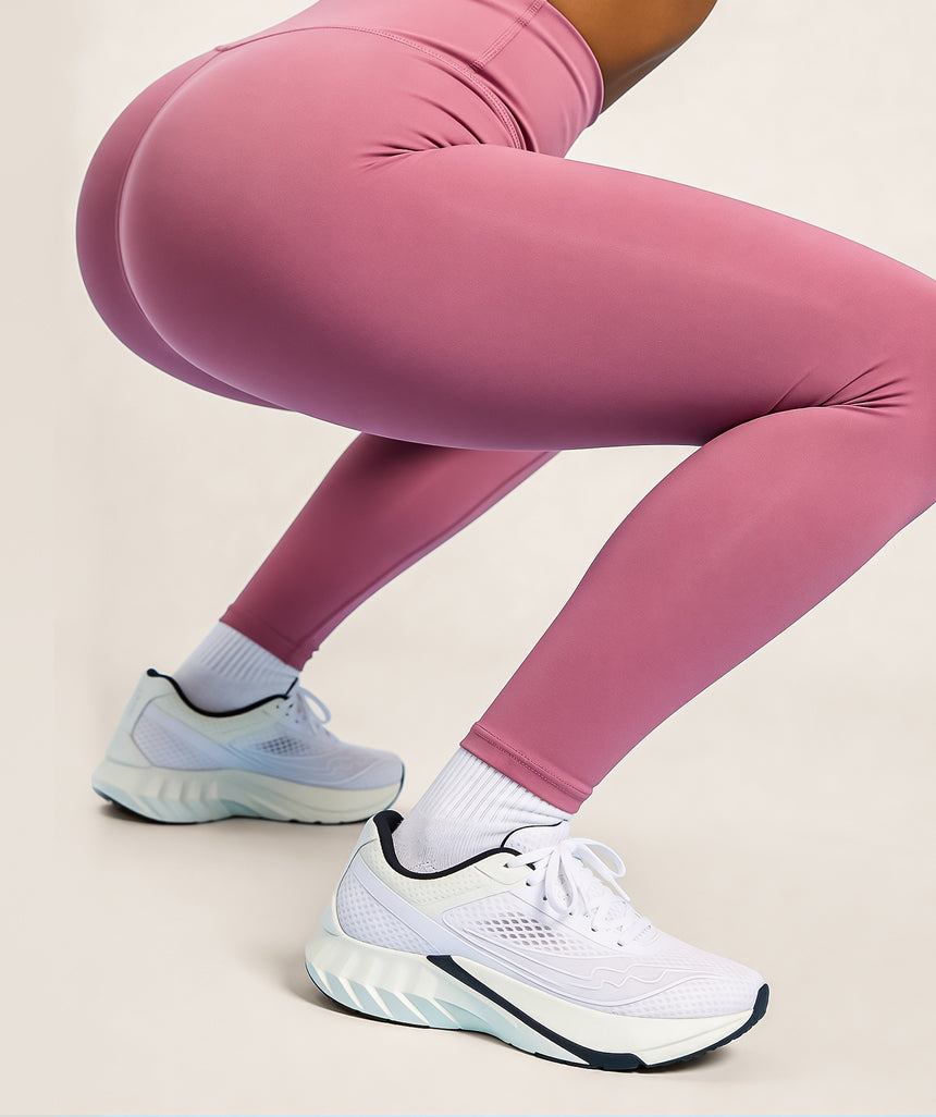 Model wearing dusty rose pink leggings and white sneakers on a beige background