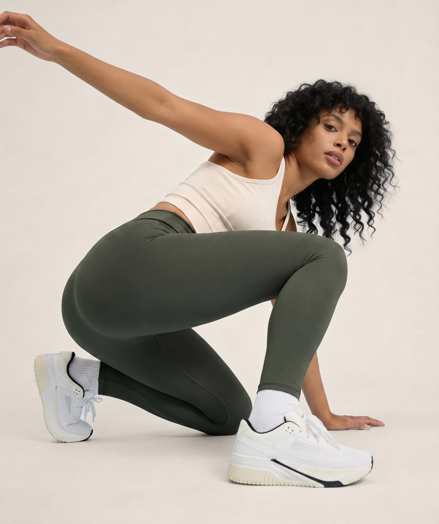 Woman in green leggings and white sneakers posing against a beige background
