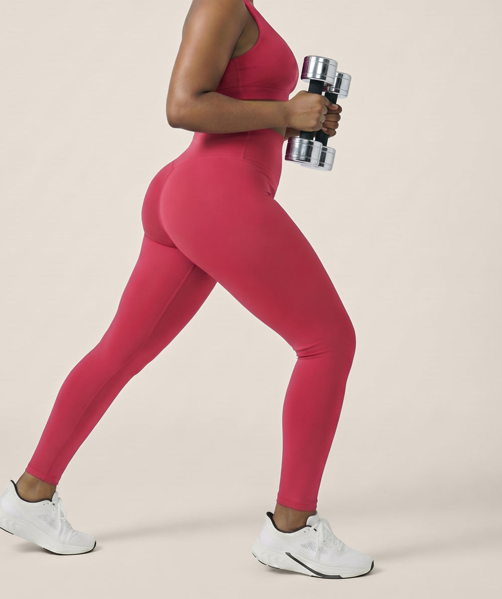 Model wearing raspberry red leggings holding a dumbbell on a beige background