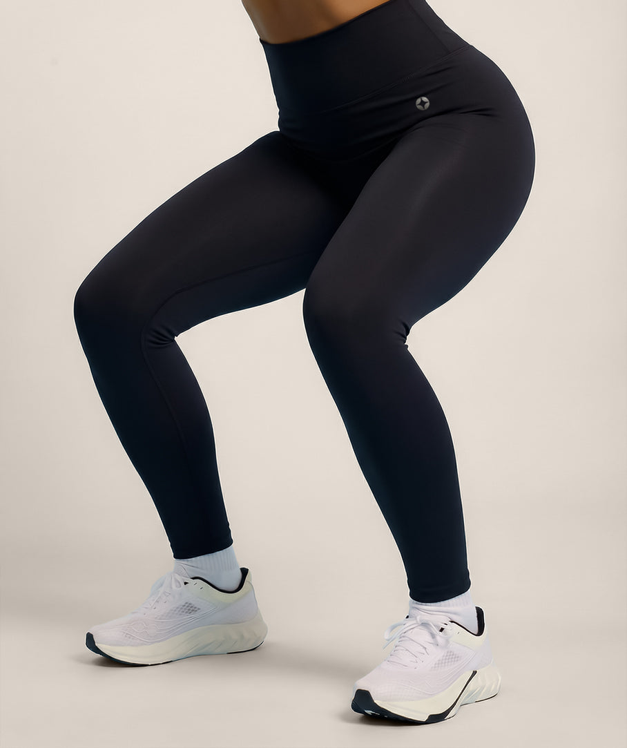 Model wearing black leggings and white sneakers on a plain background