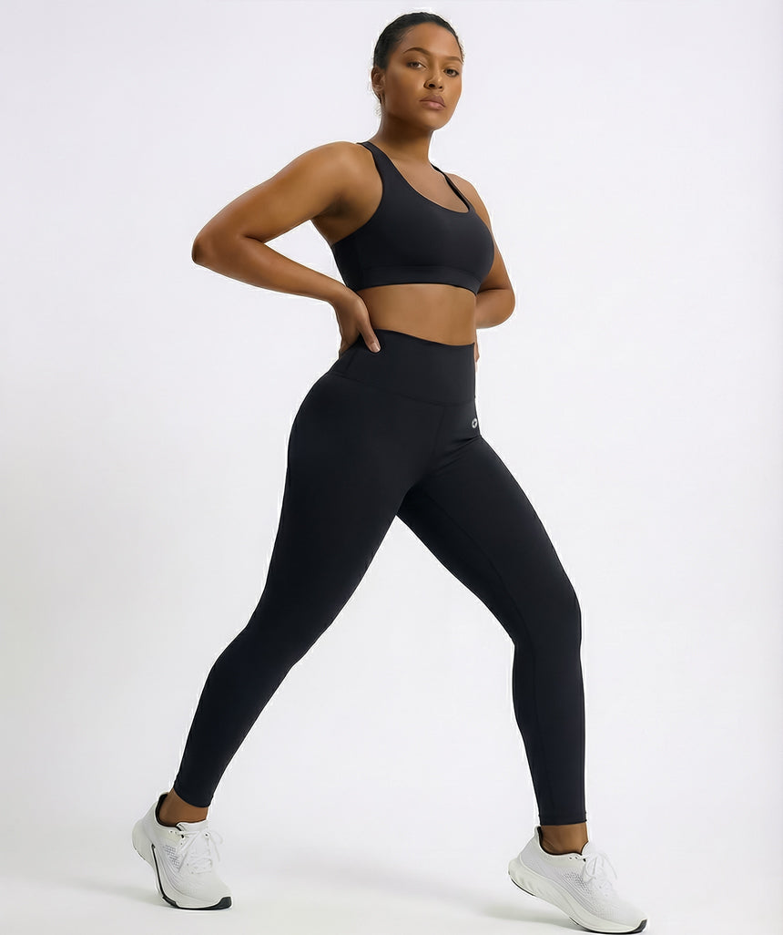 Person wearing black athletic leggings and sports bra on a white background